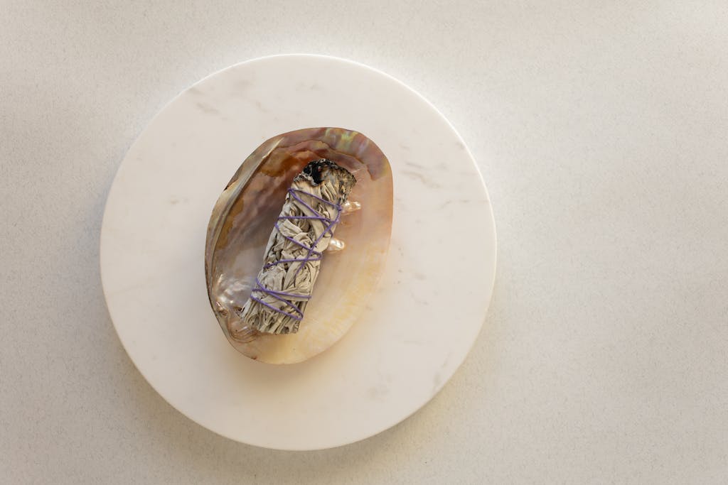 A sage smudge stick on a decorative shell placed on a marble surface, captured from above.