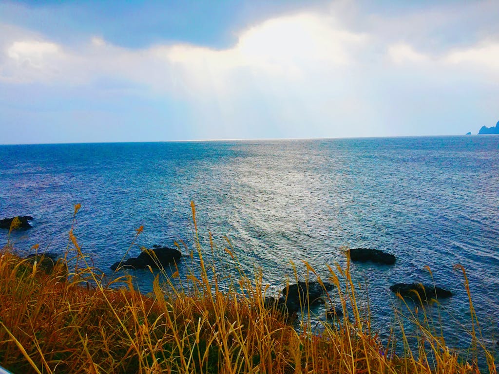 Serene ocean view from Jeju Island, South Korea, with sun rays breaking through clouds.